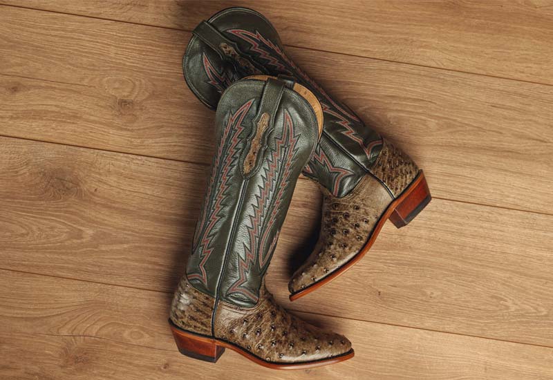A pair of the Quintana 15" Full Quill Ostrich western boot in green resting on wood.
